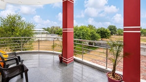 A covered outdoor area with a view of the landscape, featuring a metal railing, a potted plant, and a bench. - Collection O Salasar Balaji Temple (Sujangarh)