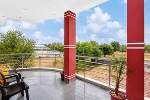 A covered outdoor area with a view of the landscape, featuring a metal railing, a potted plant, and a bench. - Collection O Salasar Balaji Temple (Sujangarh)