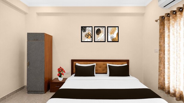 A hotel room with a bed, a wardrobe, a nightstand, a vase with flowers, and three framed artworks on the wall. - Collection O Salasar Balaji Temple (Sujangarh)