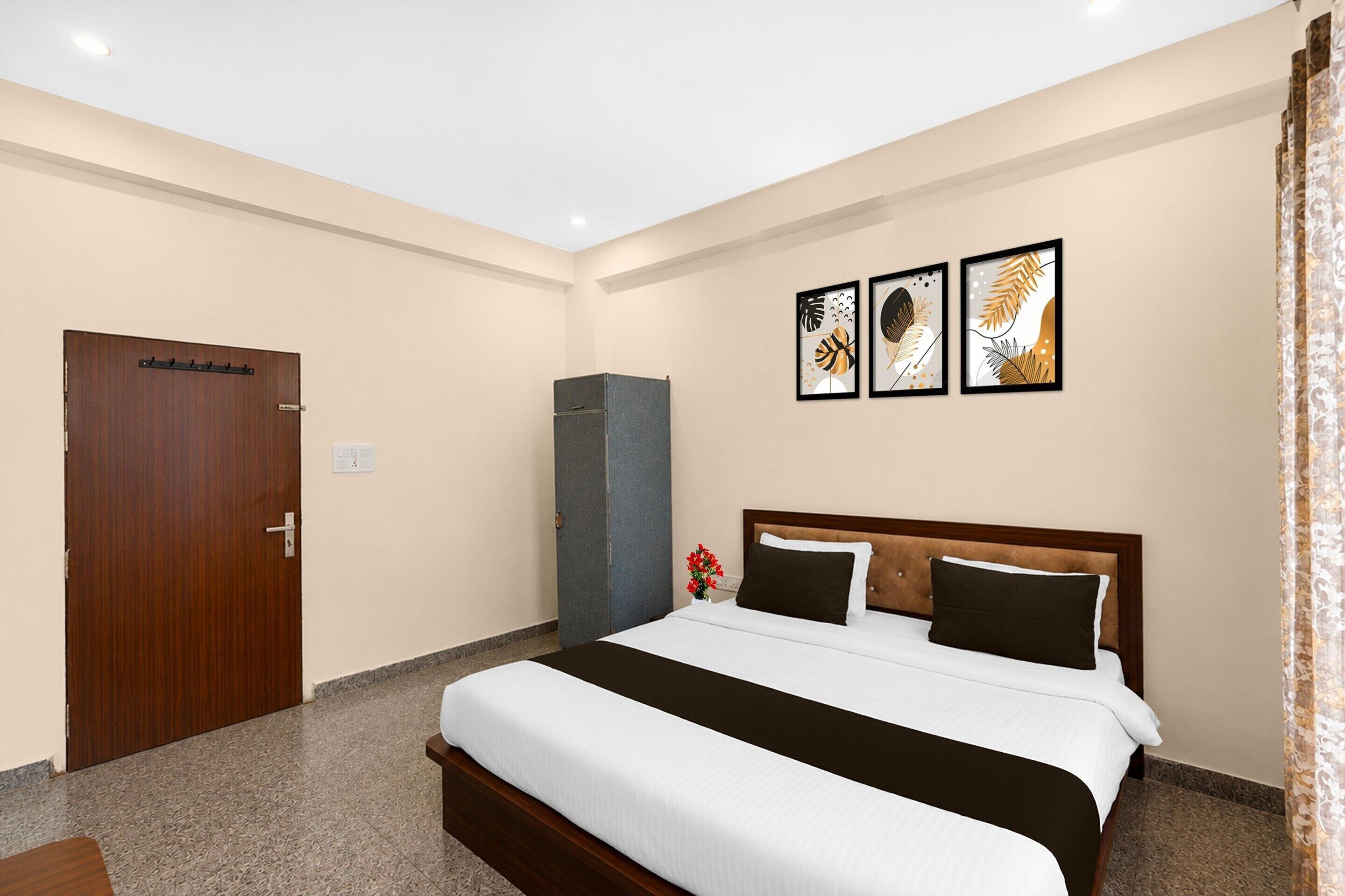 Una habitación de hotel con una cama, un armario, un pequeño mueble y tres cuadros en la pared.