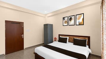 Una habitación de hotel con una cama, un armario, un pequeño mueble y tres cuadros en la pared.