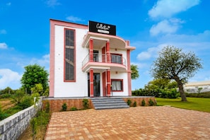A two-story building with a balcony on the second floor, a paved driveway, and a clear blue sky.