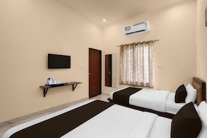 A hotel room with two beds, a flat-screen TV, an air conditioning unit, a small shelf with cups and a kettle, and a door. - Collection O Salasar Balaji Temple (Sujangarh)