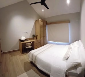 Ein Schlafzimmer mit einem Bett, einem Schreibtisch, einem Stuhl, einem Kleiderschrank und einem Deckenventilator.