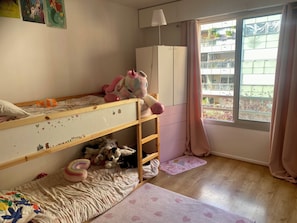 A bunk bed with toys, a white wardrobe, a window with curtains, and a view of a balcony. - Cozy Apartment in Central Paris (Paris)