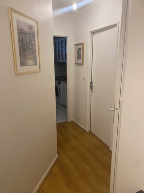 Un couloir avec un lave-linge, une porte et un tableau encadré accroché au mur.