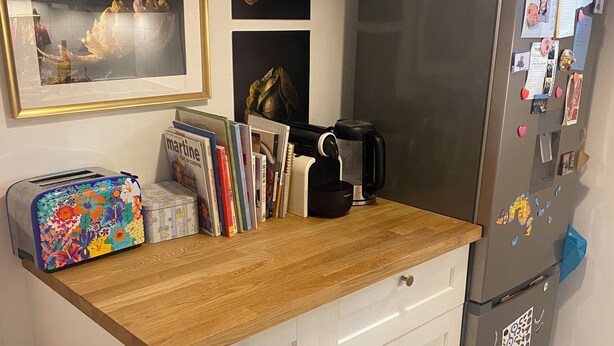 Una cocina con encimera de madera, armarios blancos, un refrigerador y diversos electrodomésticos.