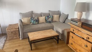 Una sala de estar con un sofá gris, una mesa de centro de madera, un aparador de madera con cajones y un radio encima.