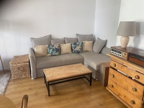 A living room with a grey sofa, a wooden coffee table, a wooden dresser with drawers, and a radio on top. - Cozy Apartment in Central Paris (Paris)