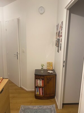 A hallway with a wooden cabinet, a clock on the wall, and a door. - Cozy Apartment in Central Paris (Paris)