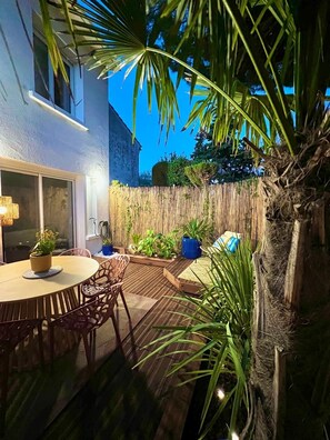 A wooden deck with a round table and chairs, surrounded by potted plants and a bamboo fence. - A cozy, quiet family home right in the heart of the city (Royan)