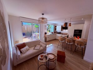 A modern living space with a sofa, dining table, and chairs, a kitchen with a dining area, and a large sliding glass door leading to an outdoor patio. - A cozy, quiet family home right in the heart of the city (Royan)