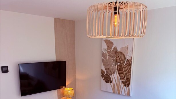 Ein modernes Wohnzimmer mit Flachbildfernseher, Holzschrank, rundem Couchtisch, Pouf in Rot, weißes Sofa und einem großen Wandbild.