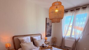 Ein Schlafzimmer mit einem großen Bett, einem Nachttisch mit Lampe, einer Pendelleuchte und einem Fenster mit Vorhängen.