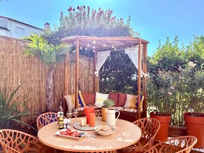 A patio with a wooden table, chairs, a cushioned bench, and a pergola with hanging lights. - A cozy, quiet family home right in the heart of the city (Royan)