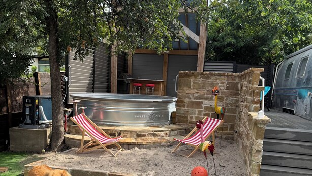 Un patio trasero con un jacuzzi, dos sillas de playa a rayas, un perro y una pelota roja.