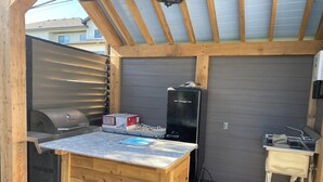 Un área de cocina al aire libre con una parrilla, refrigerador y pileta.