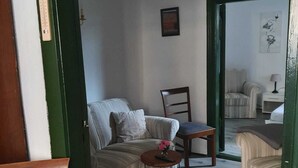 Ein Zimmer mit einer Couch, einem Sessel, einem kleinen Tisch mit einer Vase und einem Spiegel, der einen weiteren Raum reflektiert.