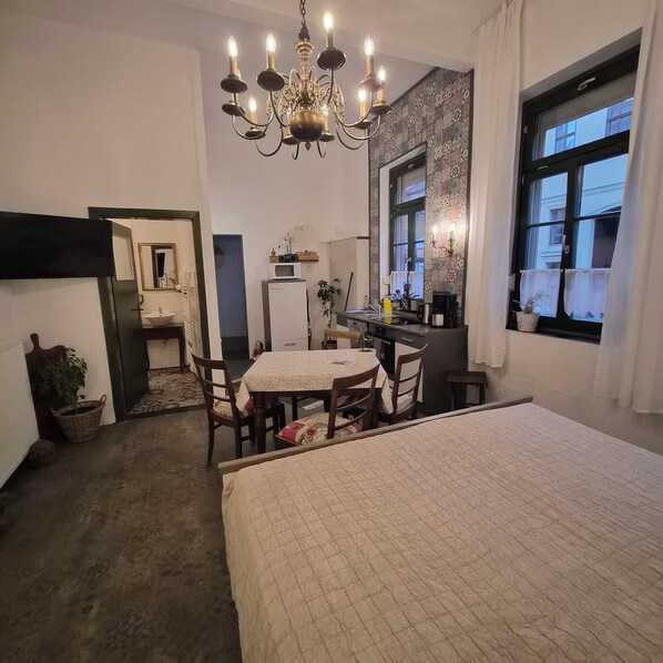 Een gezellige kamer met een bed, een eettafel, een kitchenette en een groot raam.