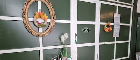 A green and white building facade with a door labeled 'HOME,' a wooden bench, a small table with a bottle and papers, and a decorative wreath.