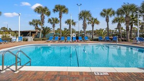Une piscine à l’eau bleue, entourée de palmiers et de chaises longues bleues.