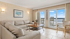 Un salon spacieux avec un canapé beige, une table basse en bois et un balcon offrant une vue sur la mer.