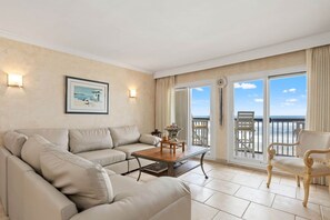 Ein geräumiges Wohnzimmer mit einem beigefarbenen Sofa, einem Holztisch und einem Balkon mit Meerblick.