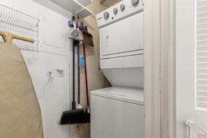 A laundry room with a stacked washer and dryer, a drying rack, and cleaning tools. - Pinnacle Port, C3-501 (Panama City Beach)