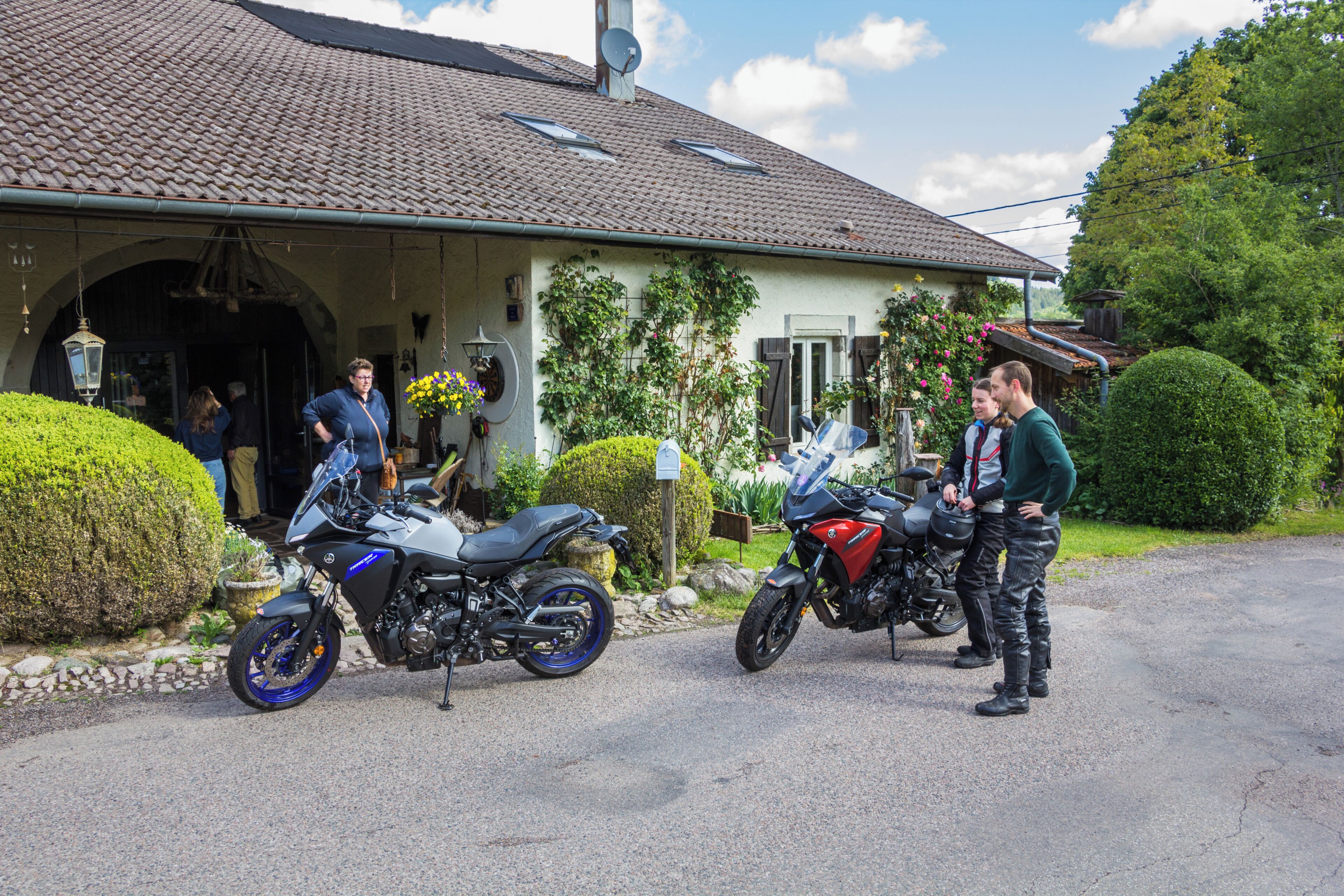 Een woonhuis met een oprit, twee motorfietsen ervoor en een verzorgde tuin.