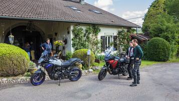 Een woonhuis met een oprit, twee motorfietsen ervoor en een verzorgde tuin.