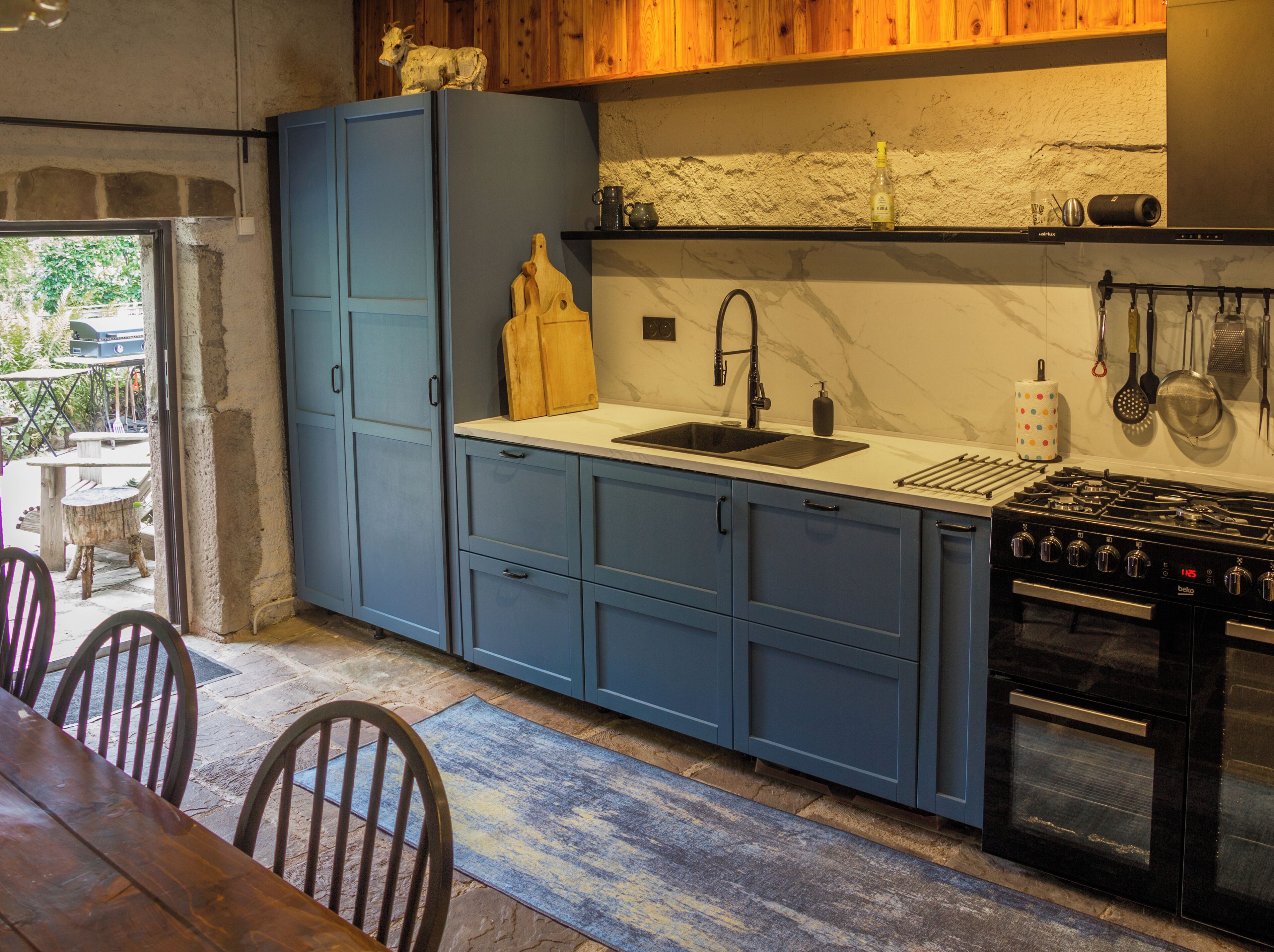 Une cuisine avec des meubles de rangement bleus, une cuisinière à gaz et un évier.