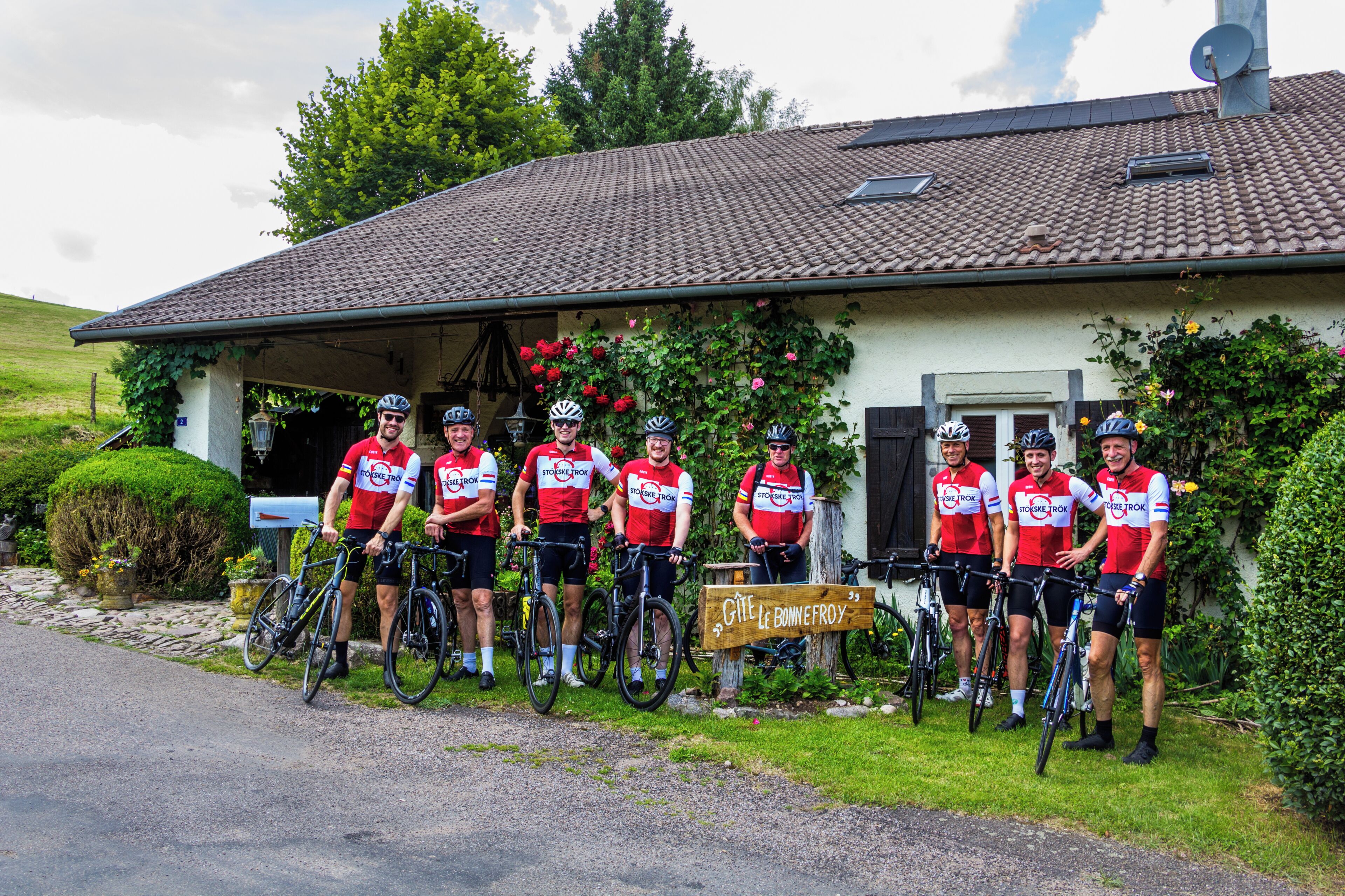 Un groupe de cyclistes se trouve devant un bâtiment dont le toit est recouvert de tuiles et sur lequel on peut lire l’inscription « Gîte Le Bonnefroy ».