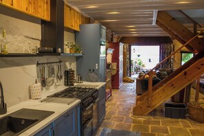 A kitchen with a stone floor, wooden beams, and a staircase leading to a living area. - Vacation rental near the Mille Etangs region and the Vosges Mountains (Corravillers)