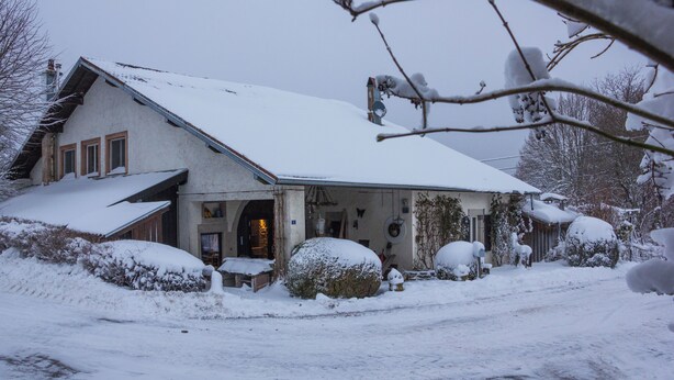 Una casa coberta de neu amb teulada inclinada, entrada visible i antena parabòlica.