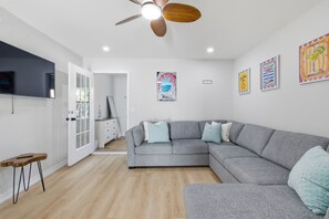 A modern living room with a grey sectional sofa, a wooden coffee table, a ceiling fan, and wall art. - ABC Private triplex near the beach and 5 ave South 6-bedroom 3-bath in Bayshore (Naples)