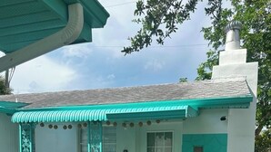 Un bâtiment à la façade blanche, agrémenté de touches de couleur turquoise, doté d’une entrée abritée et d’un petit jardin planté.