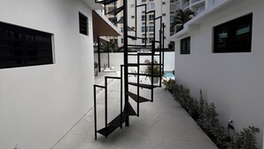 Un camí estret que porta a un edifici de disseny modern, amb una estructura metàl·lica negra, parets blanques i un cel clar.