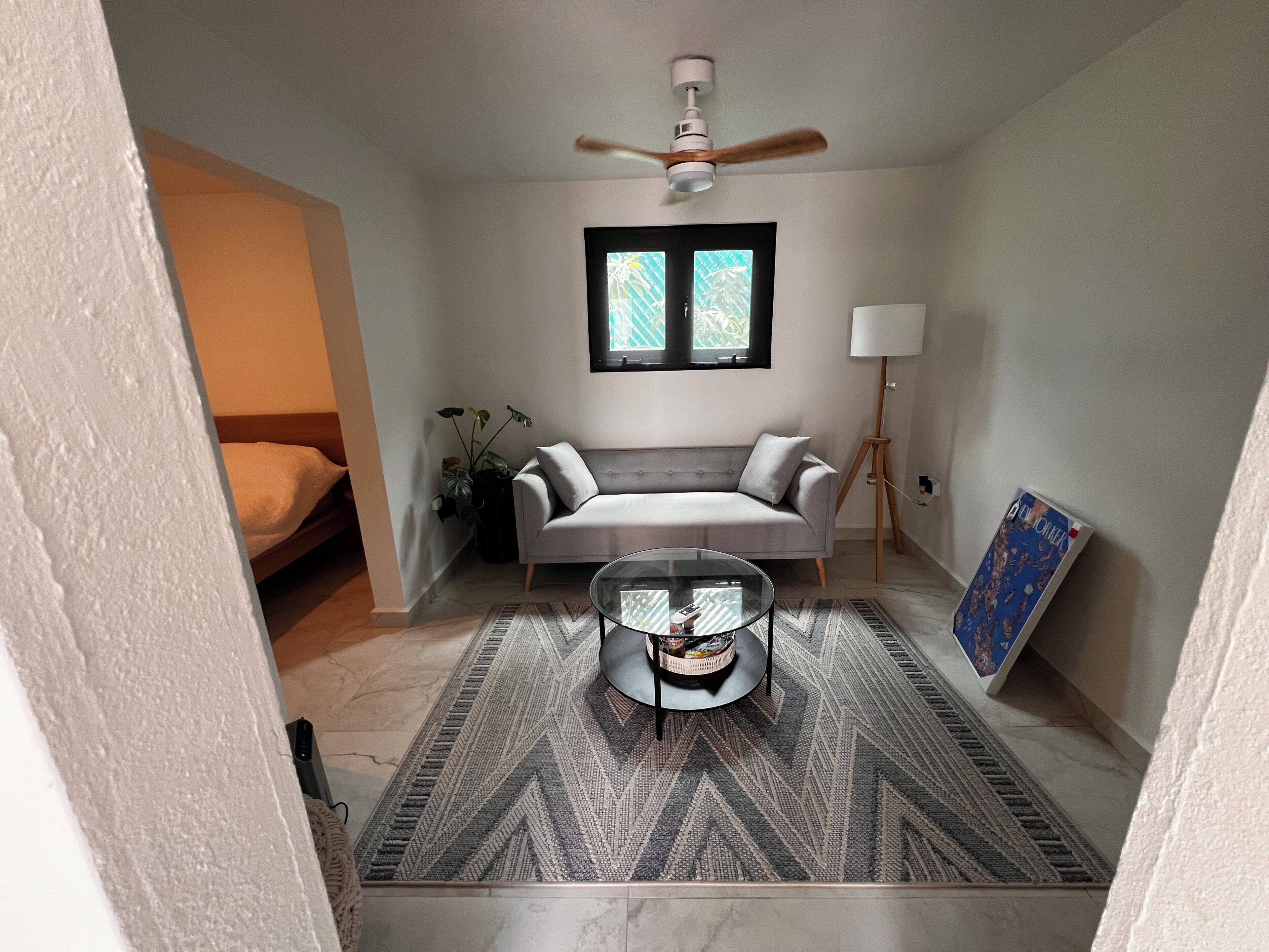 A living room with a sofa, a coffee table, a floor lamp, a ceiling fan, and a window with blinds.