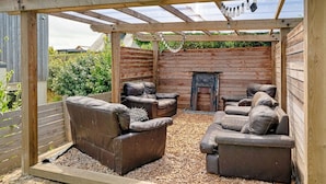 A covered outdoor seating area with a fireplace, wooden walls, and a pergola structure. - Bay House With Sea Views (Bude)