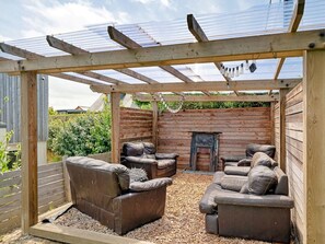 A covered outdoor seating area with a fireplace, wooden walls, and a pergola structure. - Bay House With Sea Views (Bude)