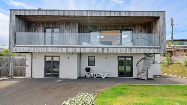 A modern two-story house with a balcony, a garage, and a small outdoor seating area. - Bay House With Sea Views (Bude)