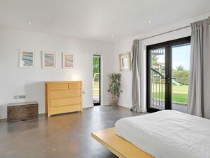 A bedroom with a bed, a wooden dresser, a potted plant, and a view of the outdoors through a sliding door. - Bay House With Sea Views (Bude)