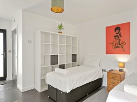 Un dormitorio con cama, armario blanco, mesita de noche, lámpara y una obra de arte en la pared.