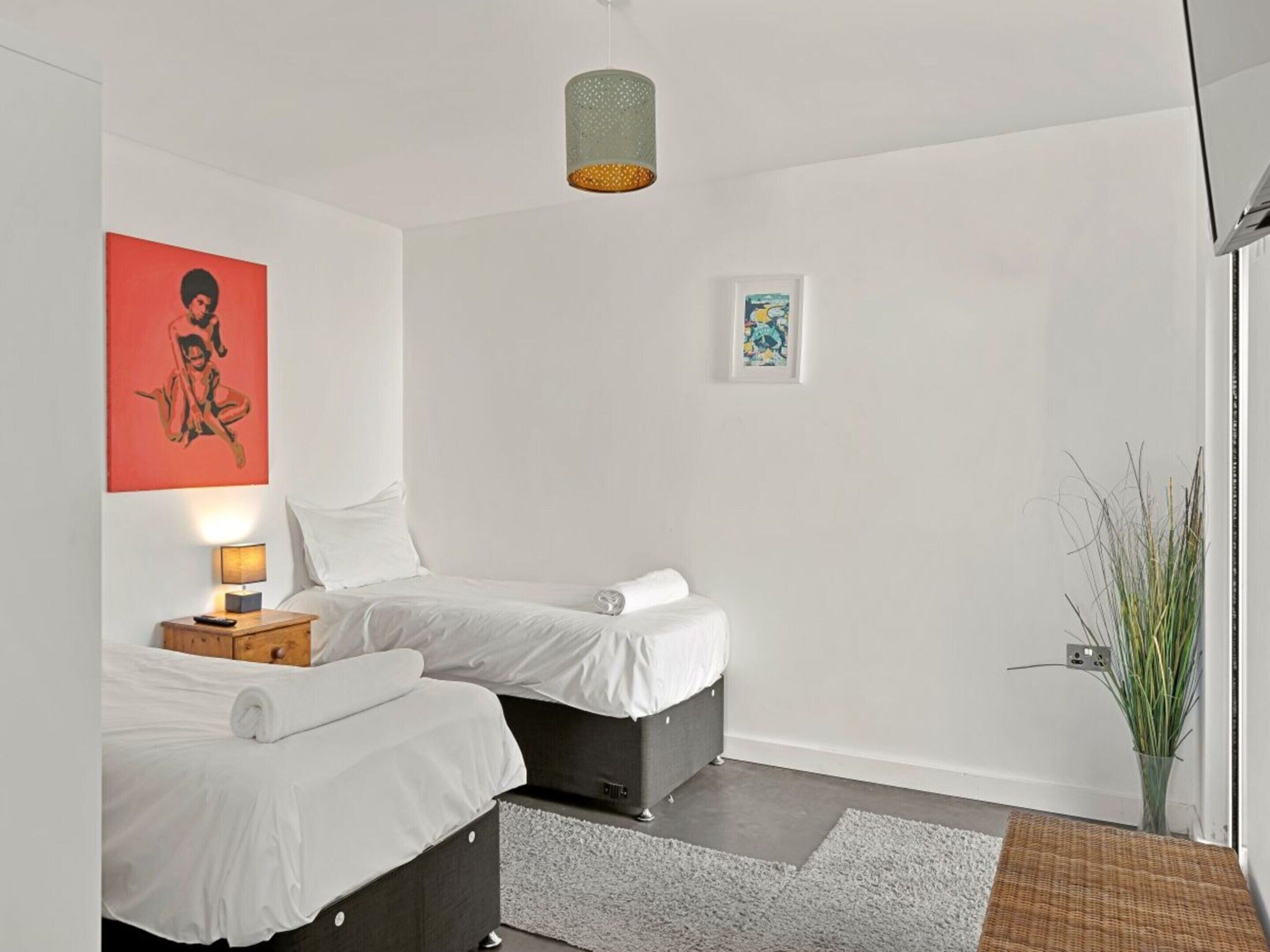 Ett hotellrum med två sängar, en lampa, en tavla och en växt.
