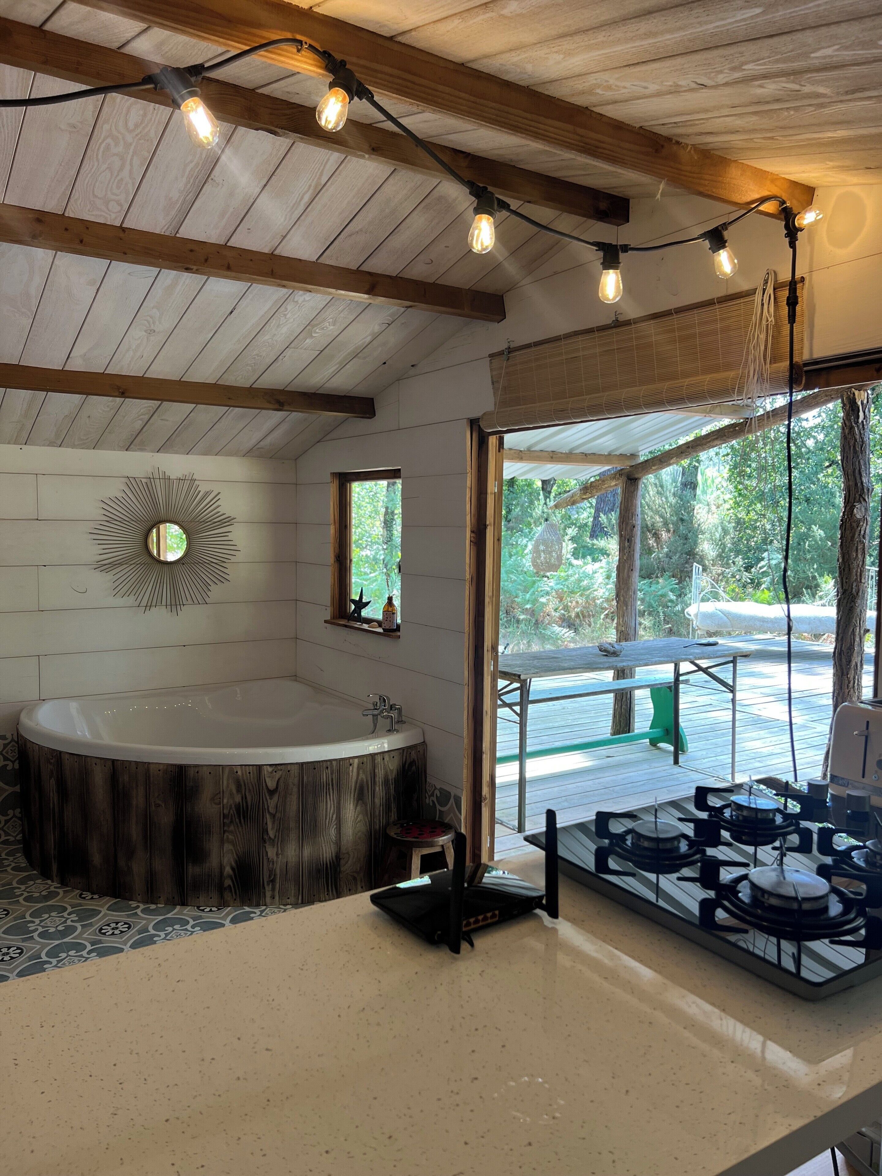 A bathroom with a wooden bathtub, a sink, and a stove. There is a window with a view of the outdoors.