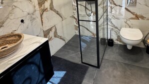 Et moderne badeværelse med en glasbrusekabine, en marmorbeklædt væg, et toilet og en vask med kumme.