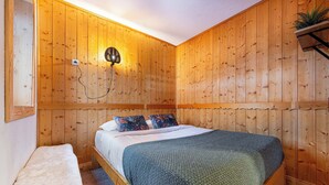 A wooden-paneled room with a bed, a bench, and a wall-mounted light fixture. - Residence Arcelle, Ski In-Out with WiFi in Val Thorens, “V1” by Versant Collection (Val Thorens)
