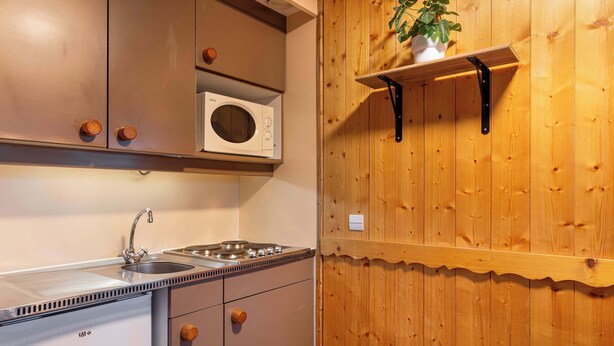 A kitchen with a microwave, sink, and stove. There is a wooden wall with a shelf and a plant. - Residence Arcelle, Ski In-Out with WiFi in Val Thorens, “V1” by Versant Collection (Val Thorens)