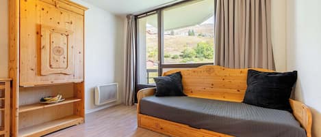 A wooden bed with a headboard, a wooden wardrobe with shelves, and a large window with curtains.