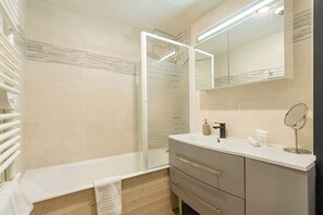 A modern bathroom with a glass shower enclosure, a vanity with a mirror, and a towel on the floor. - “V6” by Versant Collection (Val Thorens)